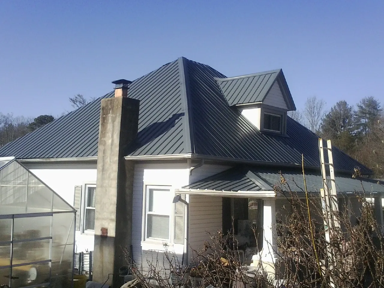 Dark blue standing seam metal roof on a white farmhouse with dormer — Slate & Tile Roof Repair by Roofing Brothers in Gloucester Point